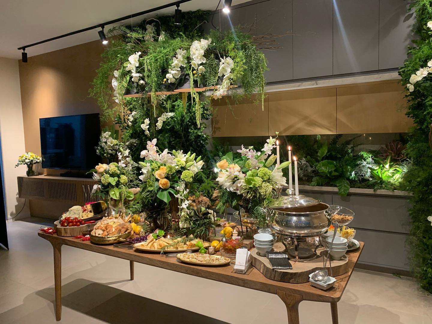 Mesa de buffet decorada com flores, folhagens e pratos preparados